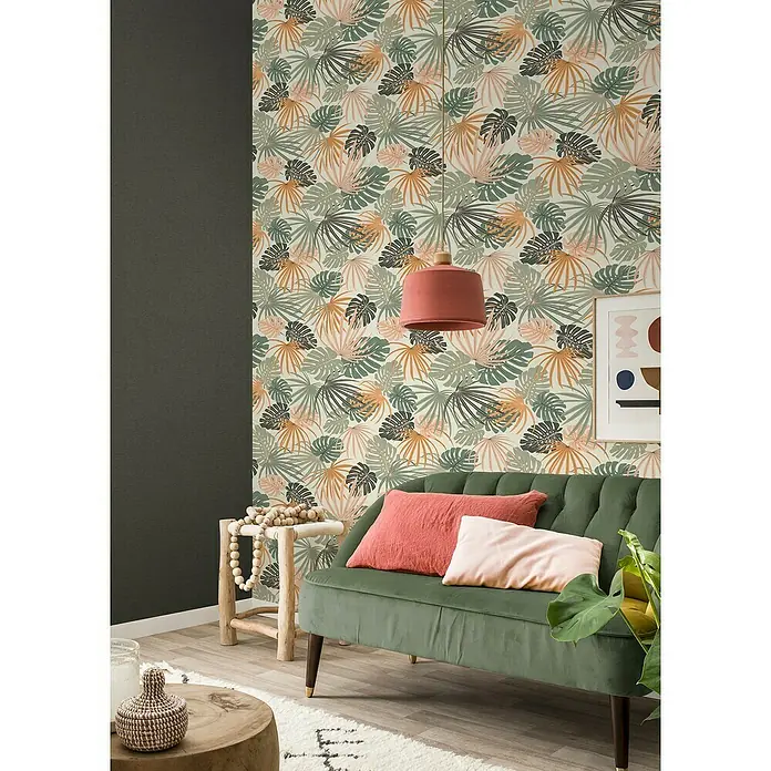 Rasch Salsa Vliestapete Blätter - Weiß-Grün, Floral, 10,05 x 0,53 m - Einladendes Wohnzimmer mit einem grünen Samtsofa, dekoriert mit Kissen, vor einer tropischen Blättertapete und ergänzt durch eine passende Hängelampe.