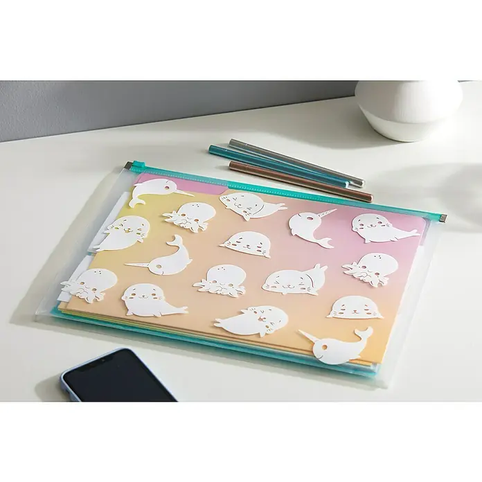 Cricut Joy Vinylfolie Smart Label - Weiß, 122 x 14 cm - Eine transparente Reißverschlusstasche mit niedlichen Meerestier-Aufklebern liegt auf einem Tisch, daneben Stifte und ein Smartphone.