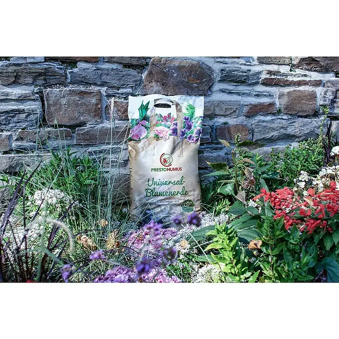 Presto Humus Bio Blumenerde für alle Zimmer- und Balkonpflanzen - 17 l - Die Presto Humus Universalerde präsentiert sich inmitten einer üppigen Blumenpracht vor einer rustikalen Steinmauer.