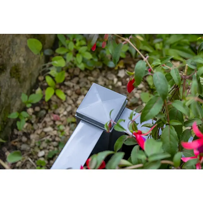 KHW Pflanzkasten - Außenmaß (L x B x H): 43 x 43 x 41 cm, Kunststoff, Grau - Nahaufnahme eines grauen Zaunpfostens mit quadratischer Abdeckung inmitten üppiger grüner Vegetation und leuchtend roter Blüten.