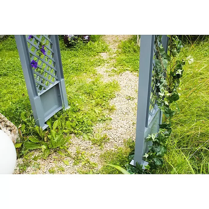 KHW Rosenbogen - Grau, 100 x 43 x 207 cm - Grauer Gartenbogen mit Spalierdesign, der einen Kiesweg in einem üppigen Garten umrahmt. Lila Blumen und grüner Efeu schmücken seine Seiten.