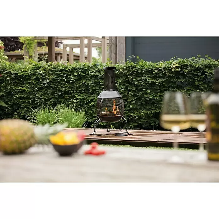 RedFire Gartenkamin Sauda - Ø x H: 38 x 90,5 cm, Stahl - Dunkle Metall-Feuerstelle mit Gitterrost und hellen Flammen, auf Holzterrasse im Garten.