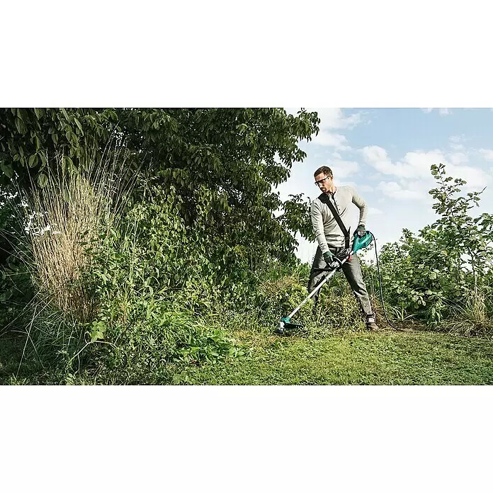 Bosch Desbrozadora de disco eléctrica AFS 23-37 - 1.000 W, Ancho de corte hilo: 37 cm, Ancho de corte cuchilla: 23 cm - Un hombre usa una desbrozadora eléctrica verde y negra para cortar hierba alta y malas hierbas en un jardín.