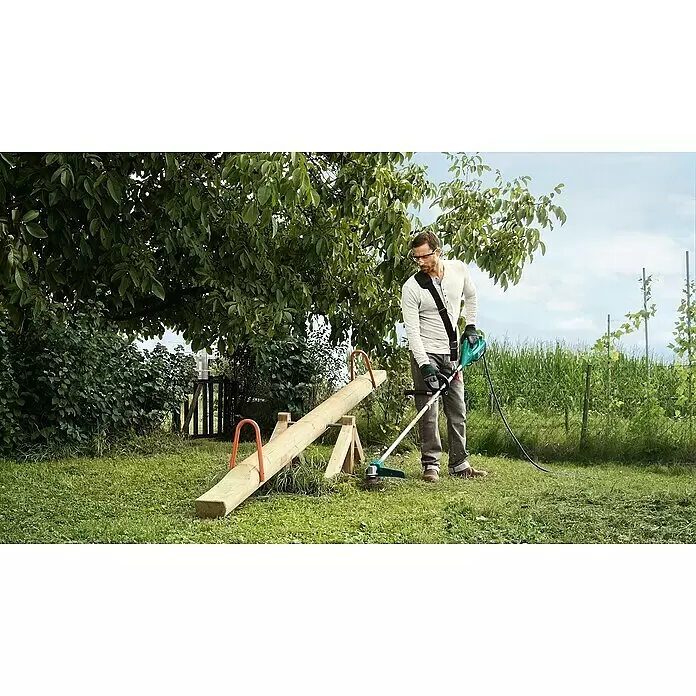 Bosch Desbrozadora de disco eléctrica AFS 23-37 - 1.000 W, Ancho de corte hilo: 37 cm, Ancho de corte cuchilla: 23 cm - Hombre usa una desbrozadora Bosch verde y negra para cortar césped alrededor de un balancín.
