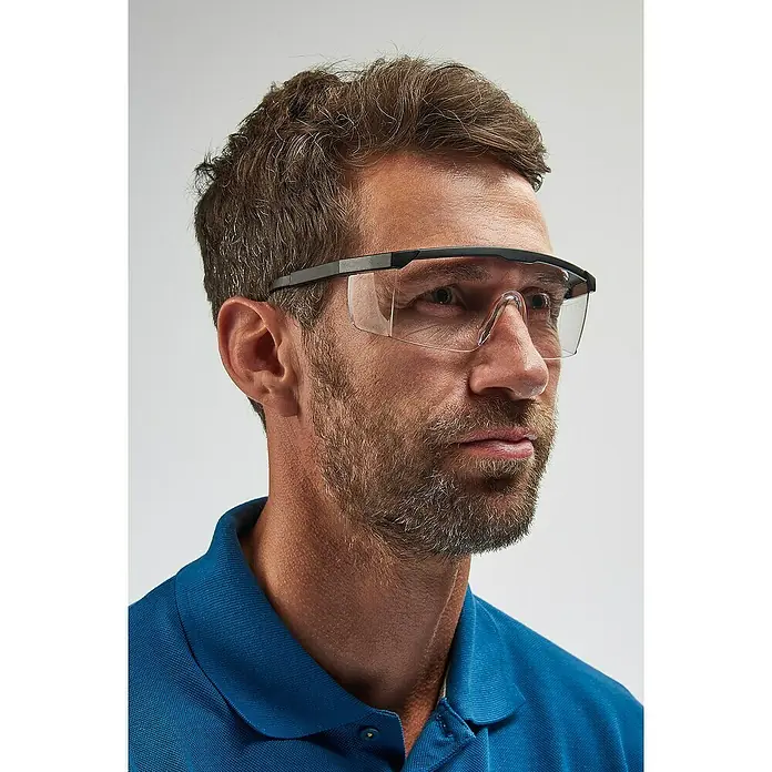 Schutzbrille - Verstellbare Bügel, Blau - Ein Mann trägt eine Schutzbrille mit schwarzem Rahmen und klaren Gläsern, die seine Augen vor Gefahren schützt. Blaue Kleidung.