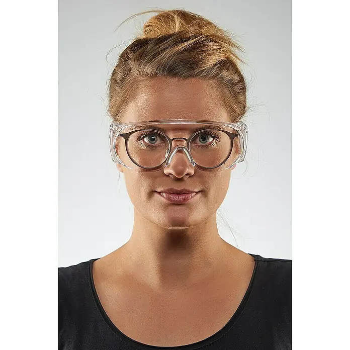 Wisent Schutzbrille - Transparent, Bügel - Eine Frau mit hochgesteckten blonden Haaren trägt eine klare Schutzbrille über ihrer normalen Brille.