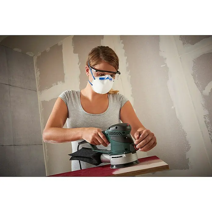 Schutzbrille - Verstellbare Bügel, Blau - Eine Frau schleift ein Stück Holz mit einem Bosch Exzenterschleifer. Sie trägt Schutzbrille und Atemschutzmaske für die Arbeit.