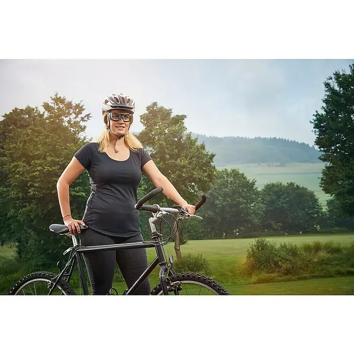 Wisent Schutzbrille - Weicher Nasensteg - Eine Frau mit Helm und Brille posiert neben ihrem Fahrrad vor einer grünen Landschaft.