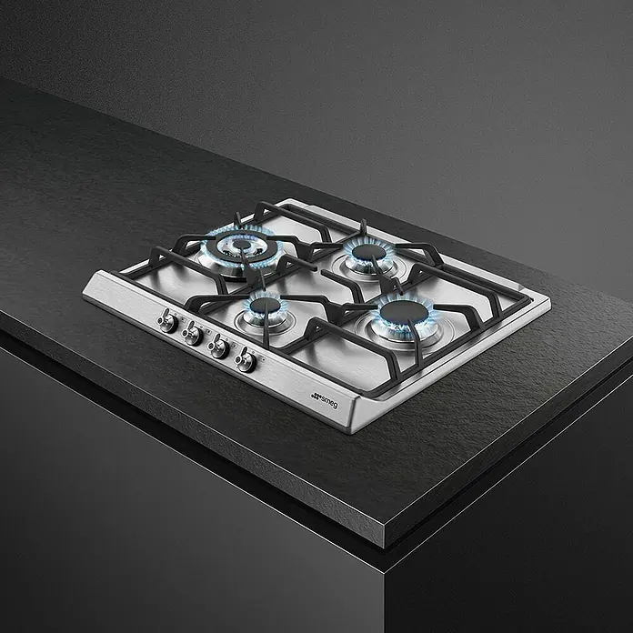 Smeg Placa de cocción de gas SER60SGH3 - L x An: 50 x 60 cm, Número de quemadores de gas: 4 ud. - Imagen de una placa de gas Smeg con cuatro quemadores sobre una encimera oscura, que muestra un diseño elegante y un rendimiento de cocción eficiente.