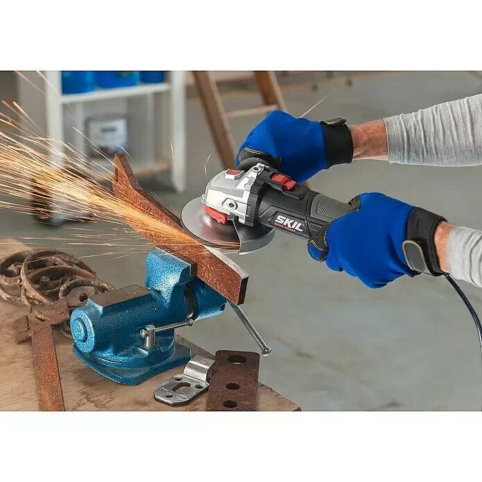 Skil Elektro-Winkelschleifer 9020 AA - 600 W, Durchmesser Scheibe: 115 mm - Person in blauen Handschuhen nutzt SKIL Winkelschleifer (grau, schwarz, rote Akzente, silberne Scheibe) um rostiges Metall zu schleifen, erzeugt Funken.