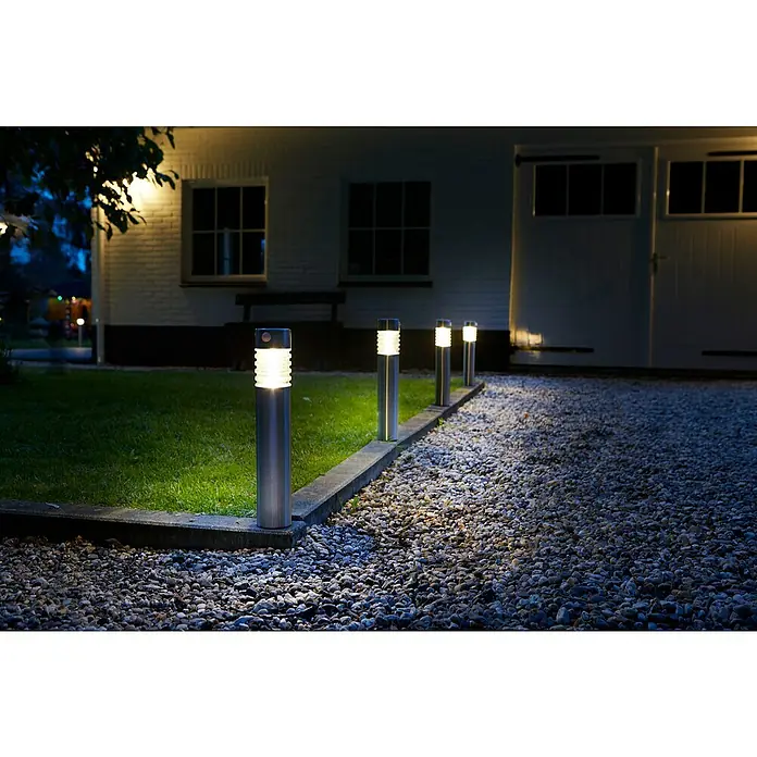 Luxform Solar Intelligent Hybrid Solar-Sockelleuchte Arizona - L x B x H: 7,6 x 7,6 x 56 cm, Silber, IP44 - Außenaufnahme von vier modernen Gartenleuchten, die einen Weg beleuchten, mit einem Haus im Hintergrund, das durch weiches Licht akzentuiert wird.