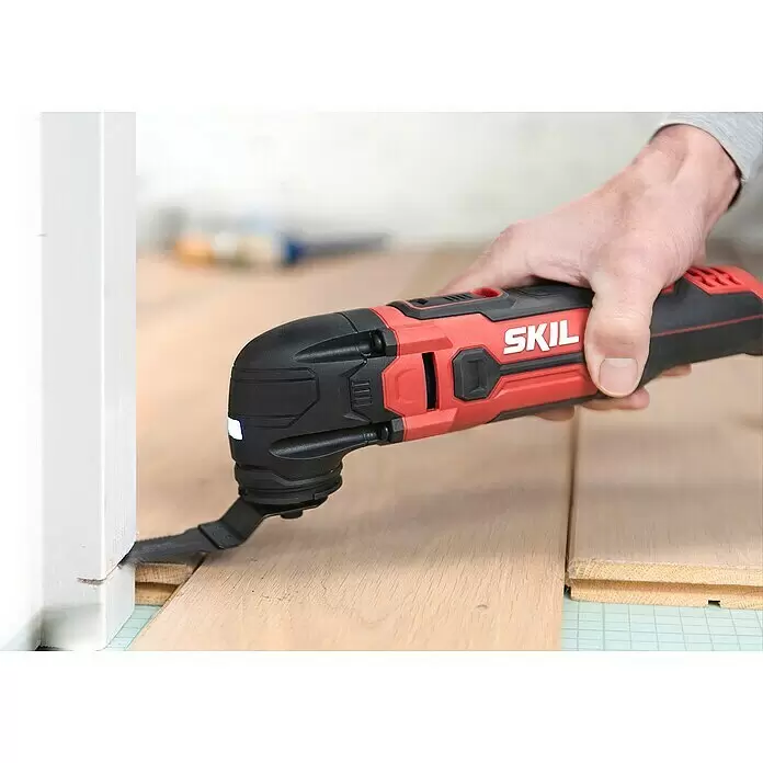 Skil Elektro-Multifunktionswerkzeug 1491 DB - 300 W - Eine Hand bedient ein rot-schwarzes SKIL Oszillationswerkzeug mit beleuchtetem Kopf, das in einen weißen Türrahmen neben Holzbrettern schneidet.
