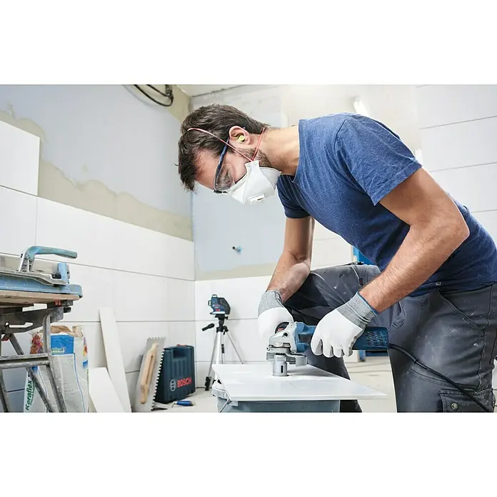Bosch Diamant-Trockenbohrer Dry Speed - Durchmesser: 20 mm - Ein Handwerker mit Schutzmaske und Handschuhen bearbeitet eine Fliese mit einem blauen Bosch-Winkelschleifer in einem Badezimmer.
