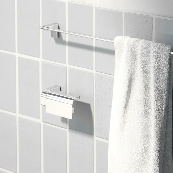Creabath Elegance Portarrollos papel higiénico - Cromo - Una toalla colgada en un toallero plateado frente a una pared de azulejos grises. En primer plano hay un portarrollos de papel higiénico.
