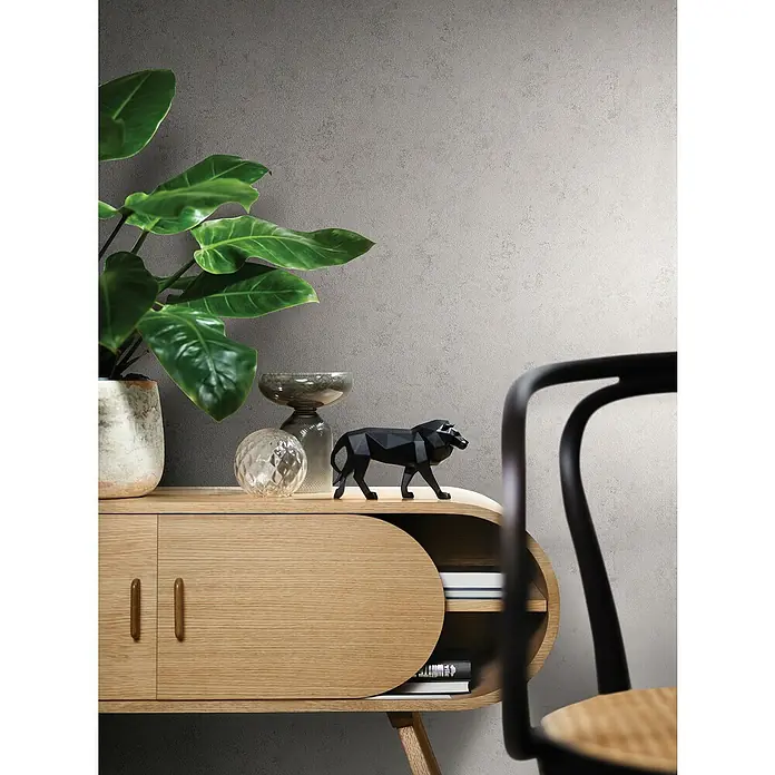 Marburg Papis Loveday Vliestapete Struktur I - Grau, Uni, 10,05 x 0,7 m - Ein stilvolles Sideboard aus hellem Holz mit abgerundeten Formen, dekoriert mit einer Pflanze, einer Glasvase und einer schwarzen Löwenfigur.