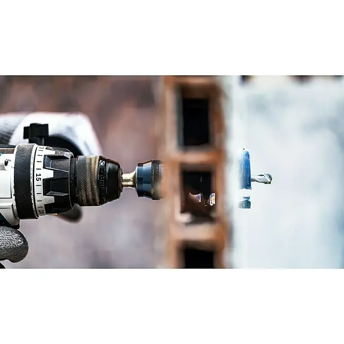 Bosch Expert Bohrmaschinenadapter - Ø x L: 7,15 x 105 mm, 2 -tlg. - Nahaufnahme einer Bohrmaschine mit einem blauen Bohraufsatz beim Bohren in eine weiße Wand. Das Werkzeug ist scharf und präzise.
