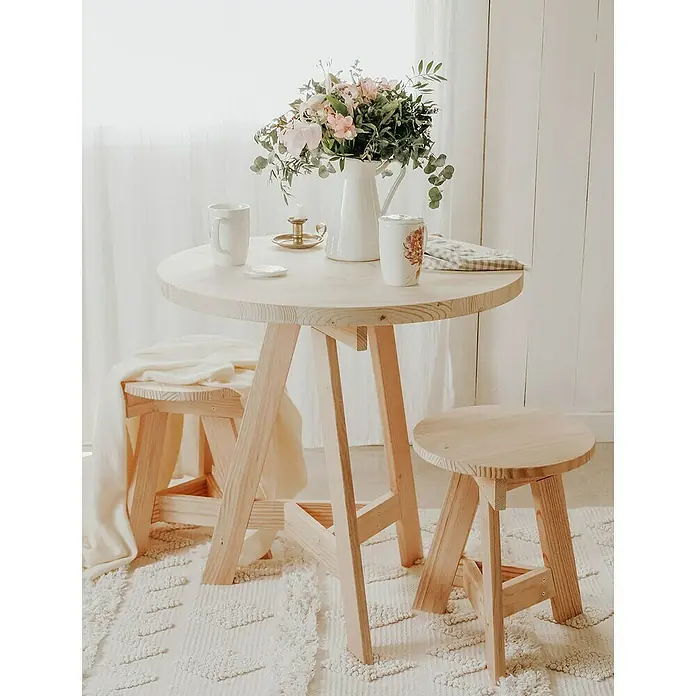 Astigarraga Tischplatte - Kiefer, Breite: 75 cm - Ein heller Holztisch mit Blumen und zwei Hockern auf einem gemusterten Teppich, der eine gemütliche, natürliche Atmosphäre schafft.