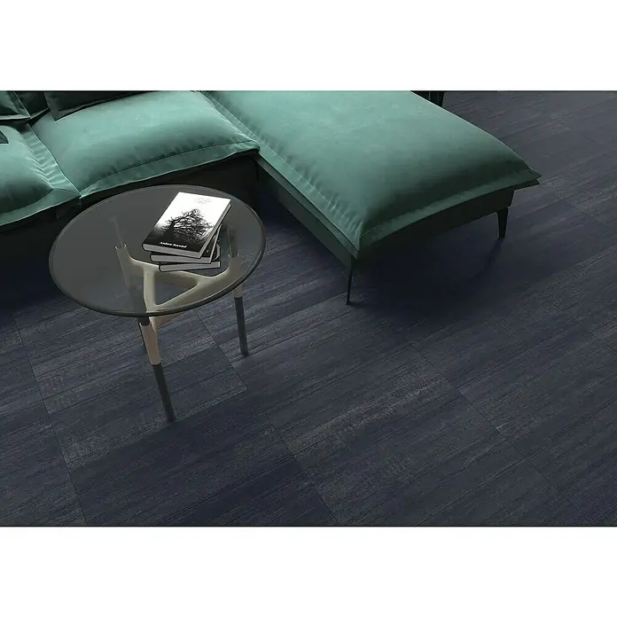 Feinsteinzeugfliese Berlin Black - 59,7 x 59,7 cm, Schwarz, Matt - Nahaufnahme eines modernen Couchtischs mit Glasplatte, auf dem Bücher liegen, neben einem grünen Sofa auf einem dunklen Holzboden.