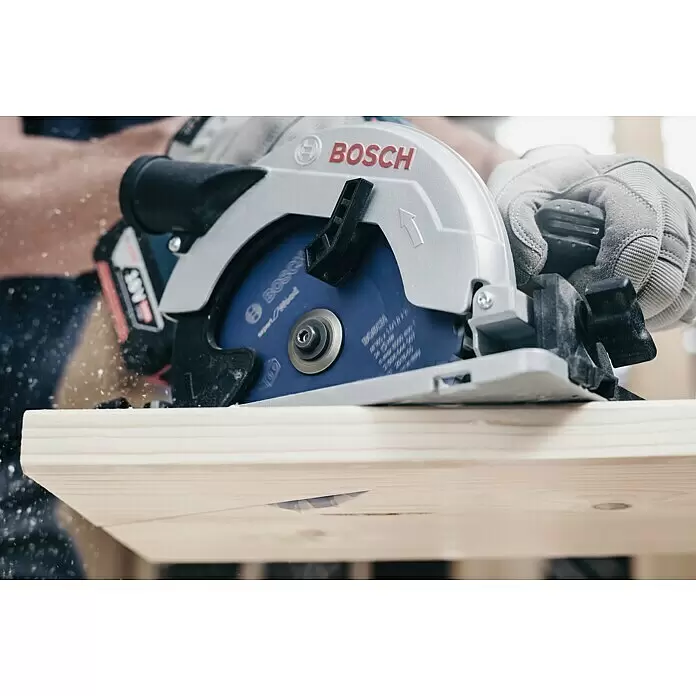Bosch Kreissägeblatt Expert for Wood - 216 mm, Bohrung: 30 mm, Anzahl Zähne: 48 Stk. - Nahaufnahme einer silber-blauen Bosch 18V Kreissäge, die ein helles Holzbrett schneidet, mit fliegenden Spänen.