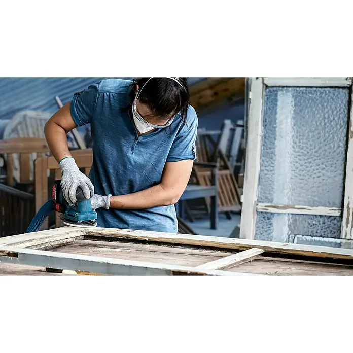 Bosch Expert Schleifblätter-Set C470 - L x B: 140 x 115 mm, 10 -tlg. - Eine Person schleift einen Holzrahmen mit einem elektrischen Schleifer, um ihn für die Restaurierung vorzubereiten, Schutzbrille tragend.