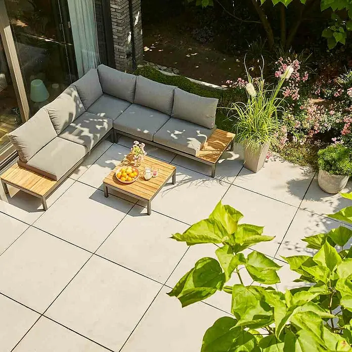 Siena Garden Loungemöbel-Set Alvida - 4 -tlg., Anthrazit/Schwarz, Teakholz, Max. Personenzahl: 5 - Eine einladende Gartensitzgruppe mit grauen Polstern und einem Holztisch, perfekt für entspannte Stunden im Freien. Dekorative Pflanzen ergänzen das Ambiente.