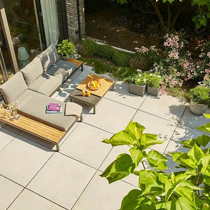 Siena Garden Loungemöbel-Set Alvida - 3 -tlg., Anthrazit/Schwarz, Teakholz, Tablett, Max. Personenzahl: 3 - Terrassenmöbel-Set mit grauem Sofa und Holztisch auf einer sonnigen Terrasse, umgeben von üppigem Grün und bunten Blumen für entspannte Stunden.