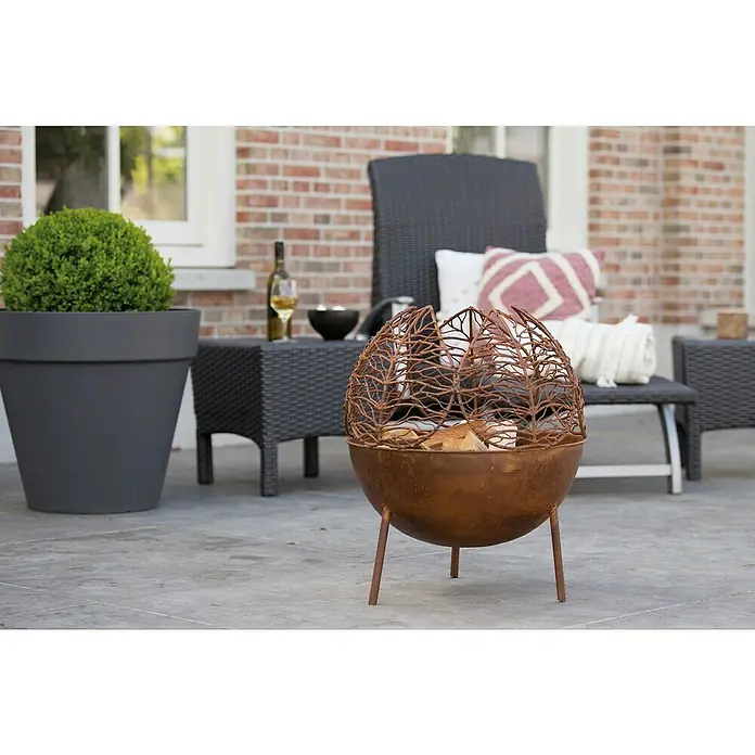RedFire Feuerkorb Narfi - Ø x H: 47 x 53 cm, Rostbraun - Eine moderne Feuerstelle mit Blattmuster, gefüllt mit Holzscheiten, steht auf einer Terrasse und schafft eine gemütliche Atmosphäre.