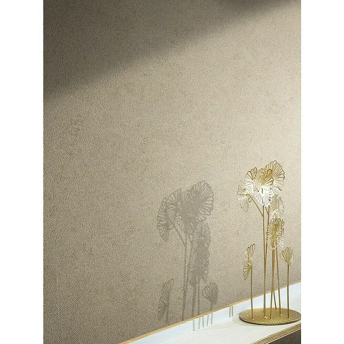 Marburg Papis Loveday Vliestapete Struktur I - Beige, Uni, 10,05 x 0,7 m - Dekorative goldene Metallblumen-Skulptur auf einem hellen Tisch mit ihrer Schattenprojektion an der Wand, die eine elegante Atmosphäre erzeugt.