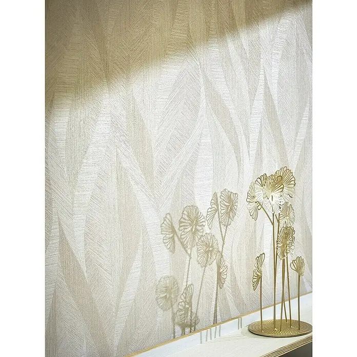 Marburg Papis Loveday Vliestapete - Beige, Wellen, 10,05 x 0,7 m - Ein dekoratives goldenes Blumenornament steht vor einer strukturierten Tapete mit Blattmuster und wirft einen zarten Schatten an die Wand.