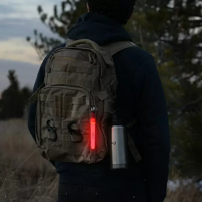 Nite Ize Barra luminosa LED mini - Rojo - Palo de luz de seguridad rojo brillante sujeto a una mochila, visto por detrás, en un entorno natural.