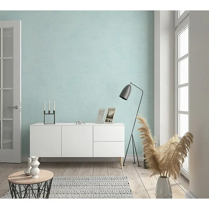 Marburg Kids' Walls Vliestapete schattiert - Helltürkis, Uni, 10,05 x 0,53 m - Wohnzimmer mit einer weißen Kommode unter einer hellblauen Wand. Eine Stehlampe und dekoratives Pampasgras stehen daneben.