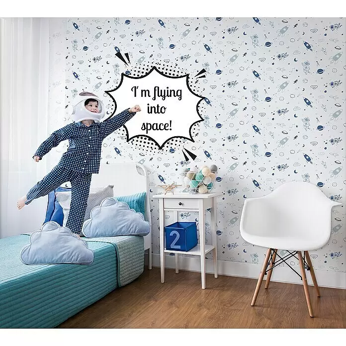 Marburg Kids' Walls Vliestapete Astronaut - Weiß/Blau, Grafisch, 10,05 x 0,53 m - Ein Kind mit Astronautenhelm und Pyjama springt auf einem Bett in einem Zimmer mit Weltraum-Tapete.