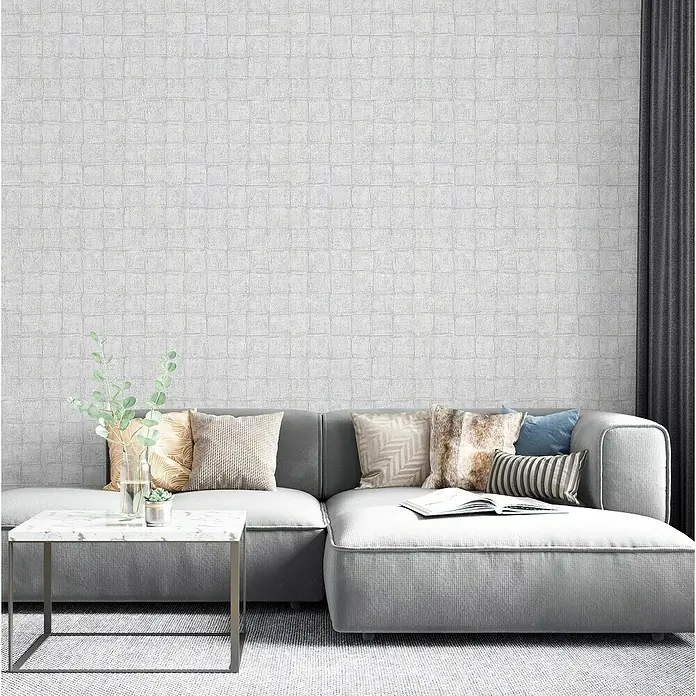 Marburg Botanica Vliestapete - Grau, Fliesenoptik, 10,05 x 0,53 m - Nahaufnahme eines modernen Wohnzimmers mit einem grauen Sofa, dekorativen Kissen, einem Marmortisch und einer strukturierten Wand.