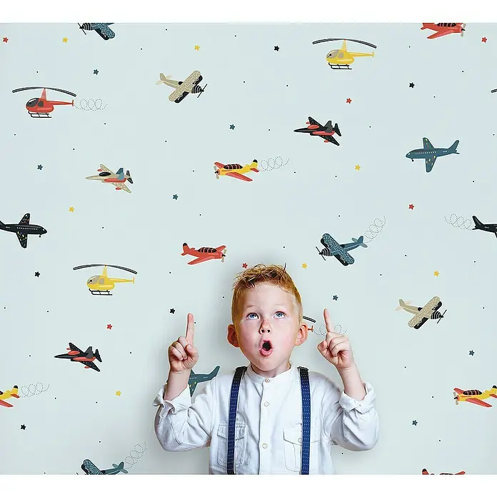 Marburg Kids' Walls Vliestapete Flugzeuge - Blau/Multicolor, Grafisch, 10,05 x 0,53 m - Ein kleiner Junge mit roten Haaren und Hosenträgern zeigt begeistert auf die Flugzeuge an der Wand. Das Kinderzimmer ist mit einem bunten Flugzeugmuster verziert.