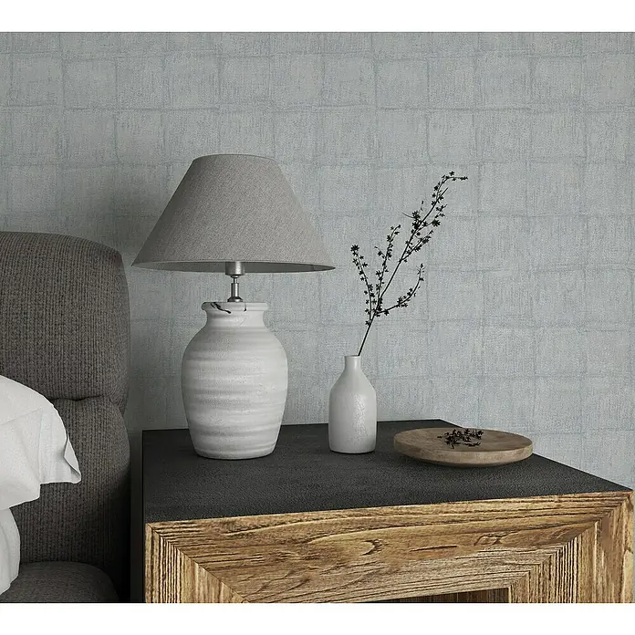 Marburg Botanica Vliestapete - Blau/Grau, Fliesenoptik, 10,05 x 0,53 m - Nahaufnahme einer Nachttischlampe mit grauem Schirm und einem kleinen Blumenstrauß in einer weißen Vase auf einem Holztisch.