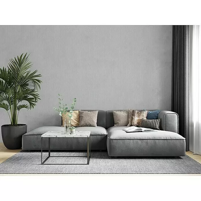 Marburg Botanica Vliestapete - Grau, Uni, 10,05 x 0,53 m - Graues L-förmiges Ecksofa mit Kissen und einem weißen Marmor-Couchtisch in einem modernen Wohnzimmer.