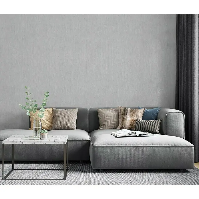 Marburg Botanica Vliestapete - Grau, Uni, 10,05 x 0,53 m - Graues modulares Ecksofa mit Kissen und Couchtisch auf einem Teppich, akzentuiert durch eine Vase mit Grünpflanzen und Vorhängen.