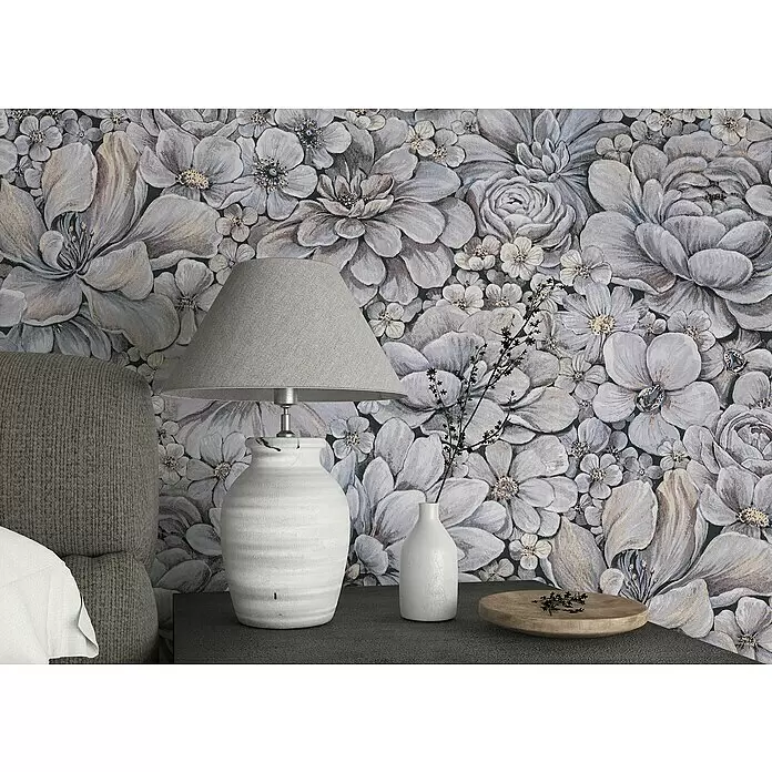Marburg Botanica Vliestapete - Grau, Floral, 10,05 x 0,53 m - Eine graue Stoff-Tischlampe mit weißem strukturiertem Keramikfuß steht auf einem Nachttisch vor einer floral gemusterten Tapete.