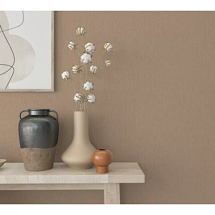 Marburg Botanica Vliestapete - Beige/Braun, Uni, 10,05 x 0,53 m - Dekovasen, Baumwollzweige und abstrakte Kunst auf hellem Holztisch vor brauner Strukturwand.