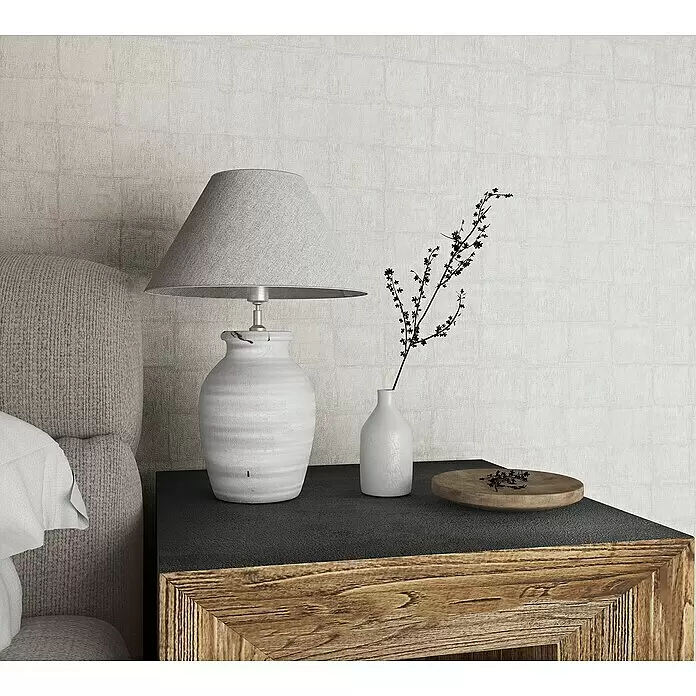 Marburg Botanica Vliestapete - Hellgrau, Fliesenoptik, 10,05 x 0,53 m - Rustikaler Nachttisch mit dunkler Platte und Holzrahmen, neben einem Bett, mit Keramiklampe und Deko-Zweigen.
