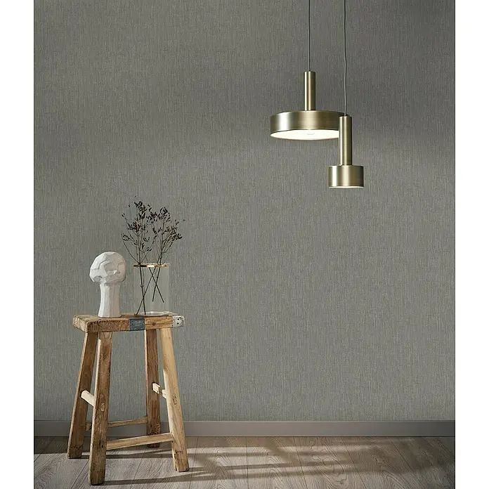 Marburg Botanica Vliestapete Struktur - Anthrazit, Uni, 10,05 x 0,53 m - Hängelampe aus Messing mit modernem Design über einem Holzhocker mit Büste und Blumen, die eine elegante Inneneinrichtung zeigt.