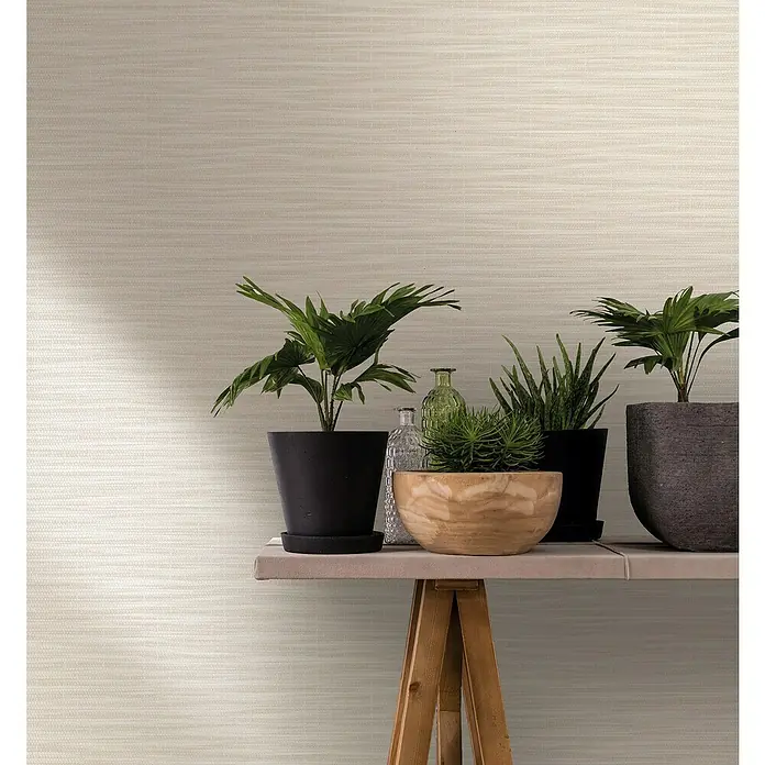 Marburg Botanica Vliestapete Webstruktur - Weiß/Beige, Uni, 10,05 x 0,53 m - Pflanzenarrangement mit verschiedenen Topfpflanzen und dekorativen Glasflaschen auf einem Tisch mit Holzgestell vor einem beigen Hintergrund.