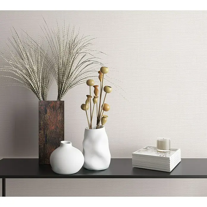 Marburg Botanica Vliestapete Struktur - Weiß, Uni, 10,05 x 0,53 m - Dekorative Vasen und Accessoires auf einem schwarzen Regal. Eine braune Vase mit Federn und eine weiße Vase mit Zweigen stehen neben einem Buchstapel mit Kerze.