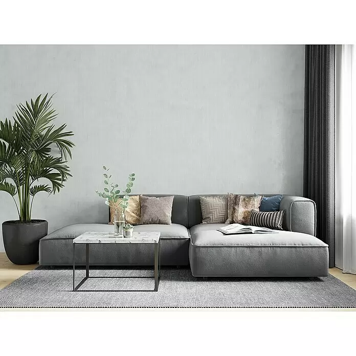 Marburg Botanica Vliestapete Struktur - Graugrün, Uni, 10,05 x 0,53 m - Ein geräumiges graues Ecksofa in einem modernen Wohnzimmer, mit Zierkissen, neben einem Couchtisch und einer großen Pflanze.