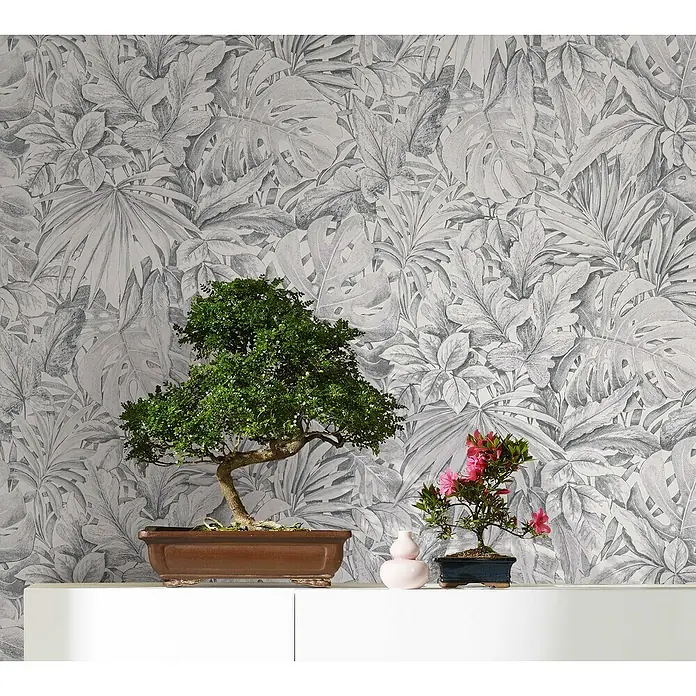 Marburg Botanica Vliestapete - Hellgrau, Floral, 10,05 x 0,53 m - Zwei Bonsai-Bäume, einer mit grünen Blättern, der andere mit rosa Blüten, stehen auf einem weißen Regal vor einer Blättertapete.