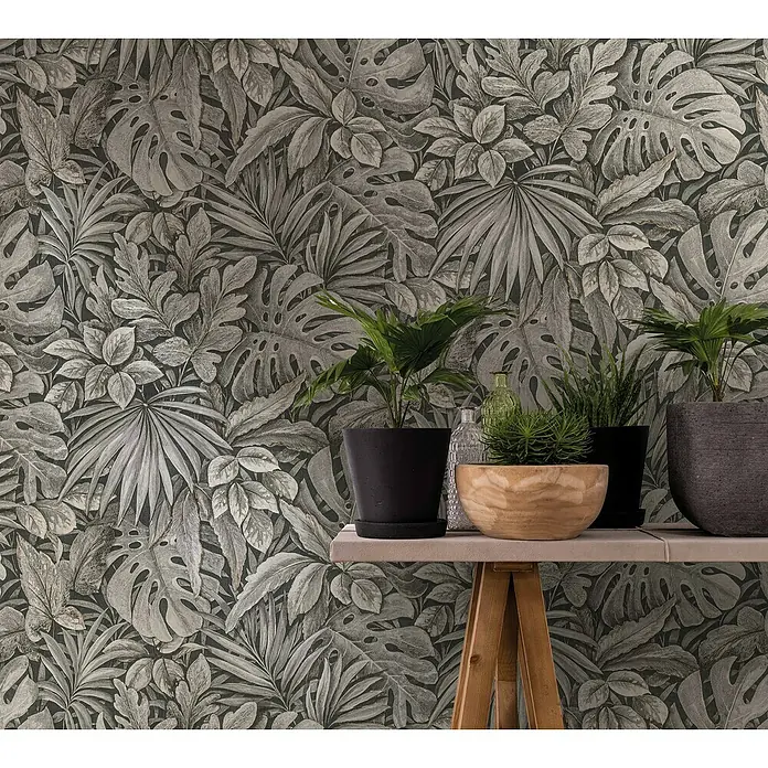 Marburg Botanica Vliestapete - Braun, Floral, 10,05 x 0,53 m - Ein stilvolles Arrangement mit Zimmerpflanzen in Töpfen auf einem Tisch, vor einer Wand mit tropischem Blätterdesign.