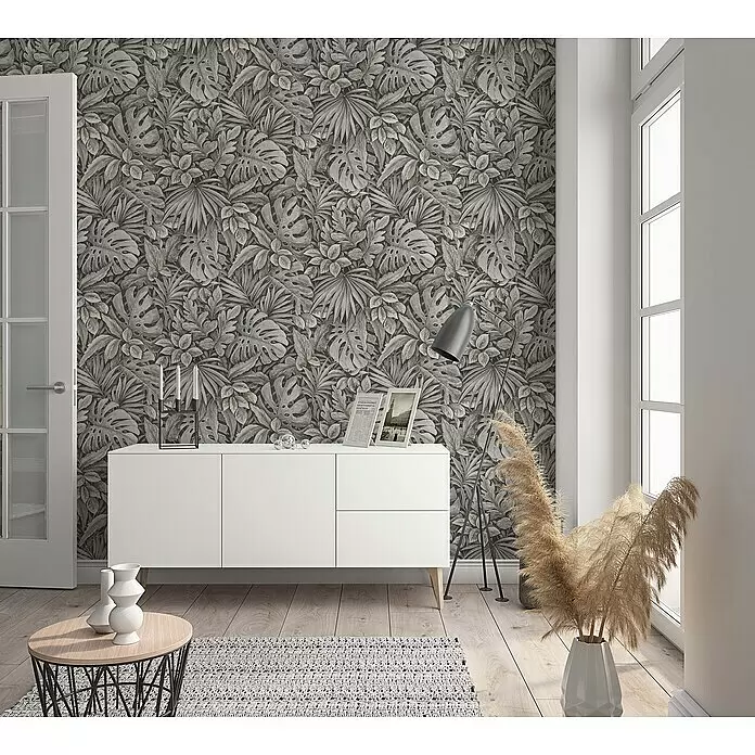 Marburg Botanica Vliestapete - Braun, Floral, 10,05 x 0,53 m - Dunkelgraue Tapete mit detailliertem tropischem Blattmuster, einschließlich Monstera- und Palmenblättern, an einer Wohnzimmerwand hinter einem weißen Schrank.