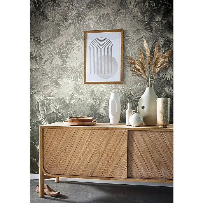 Marburg Botanica Vliestapete - Platin, Floral, 10,05 x 0,53 m - Stilvolles Sideboard aus Holz mit dekorativen Elementen und einem abstrakten Wandbild vor einer floralen Tapete.