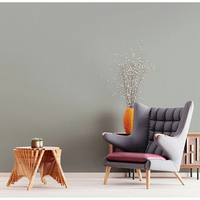 Marburg Kids' Walls Vliestapete - Mittelgrau, Uni, 10,05 x 0,53 m - Elegantes Interieur mit einem modernen, hochlehnigen Sessel in Grau und einem dekorativen Holztisch, ergänzt durch eine orangefarbene Vase mit Zweigen.