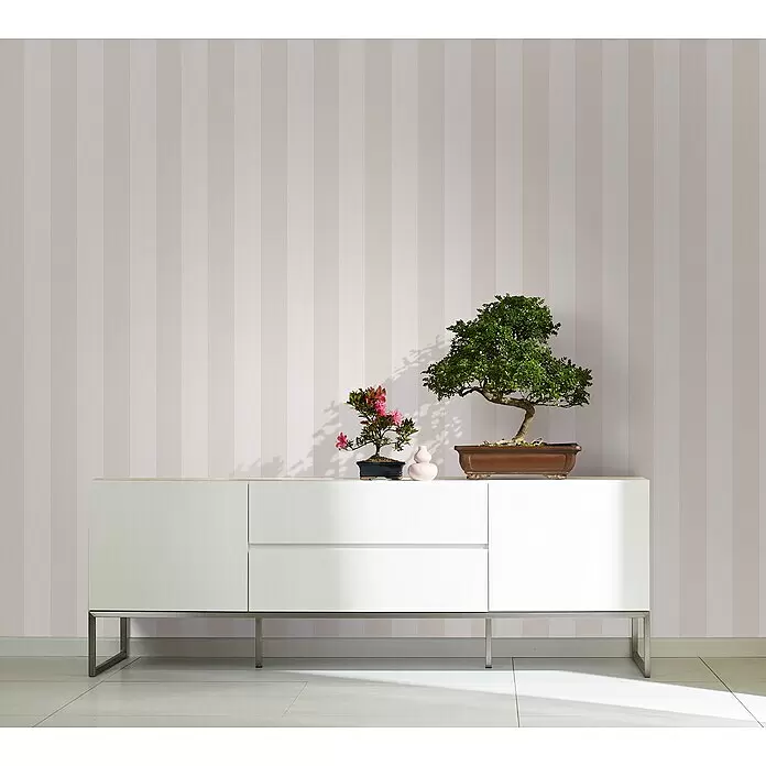 Marburg Kids' Walls Vliestapete - Beige/Weiß, Streifen, 10,05 x 0,53 m - Weißes, modernes Sideboard mit Metallbeinen, auf dem zwei Bonsai-Bäume und eine kleine Vase stehen, vor einer gestreiften Wand.
